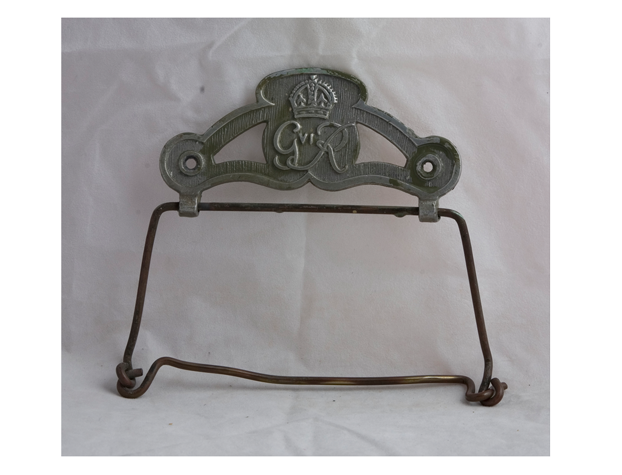 A toilet roll holder, with the letters 'GR' and a crown engraved in the grey metal part of the holder.