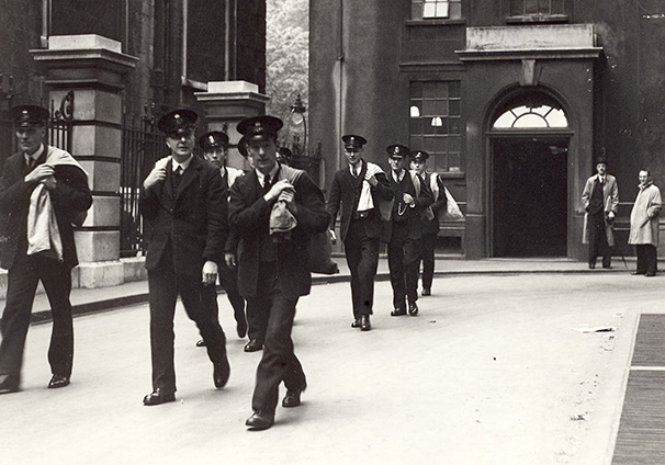 London Postmen - leaving King Edward Building on delivery. A group of postmen, carrying bags over their shoulders, leave King Edward Building to begin their deliveries.