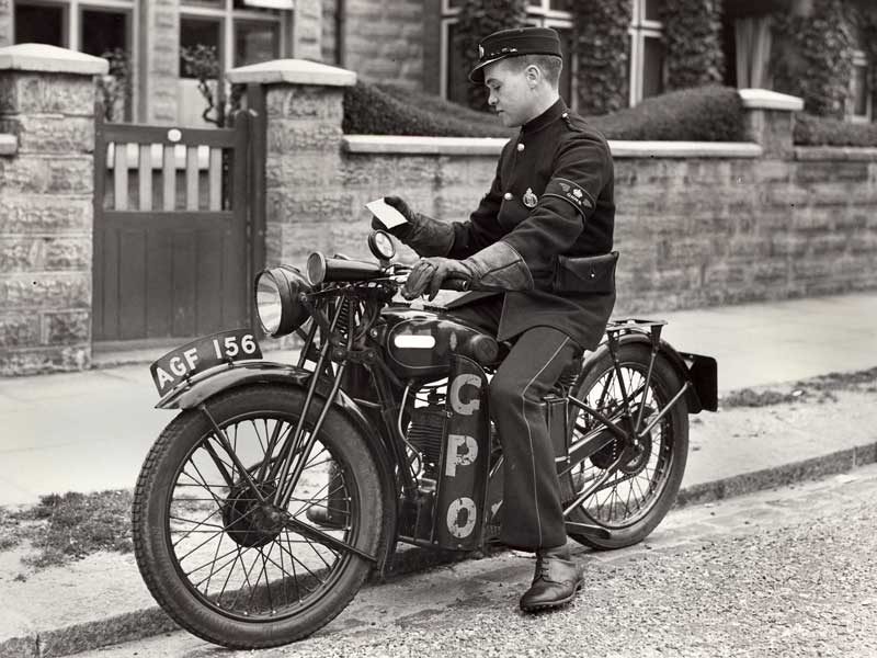 Black and white photograph of a boy on a motorcycle outside of a house.