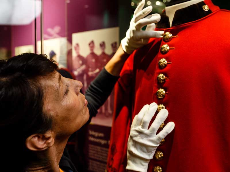 A conservator working on a red coach guard uniform in The Postal Museum exhibition.