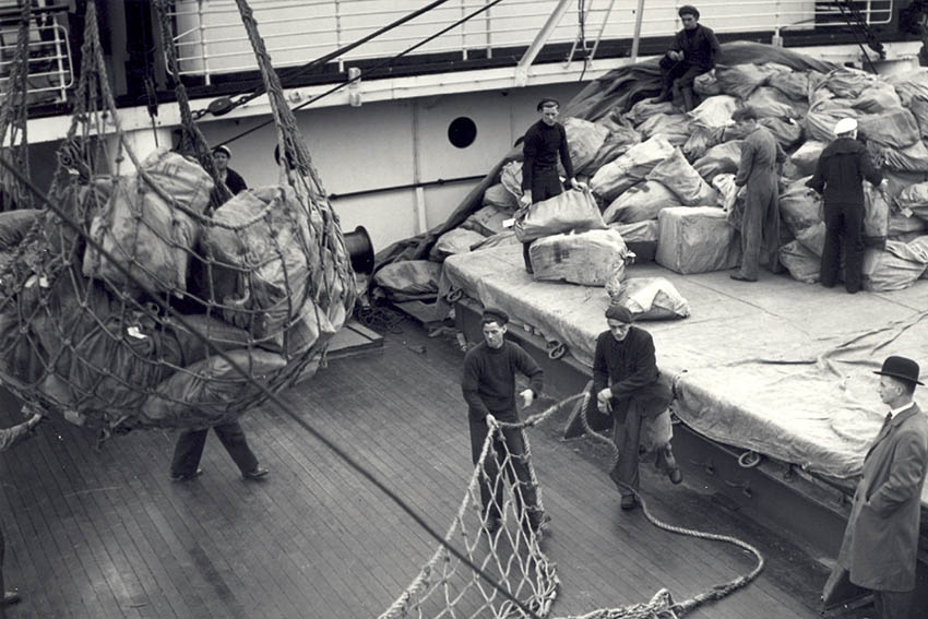 A scene of mail being unloaded from a ship in the early 20th century.