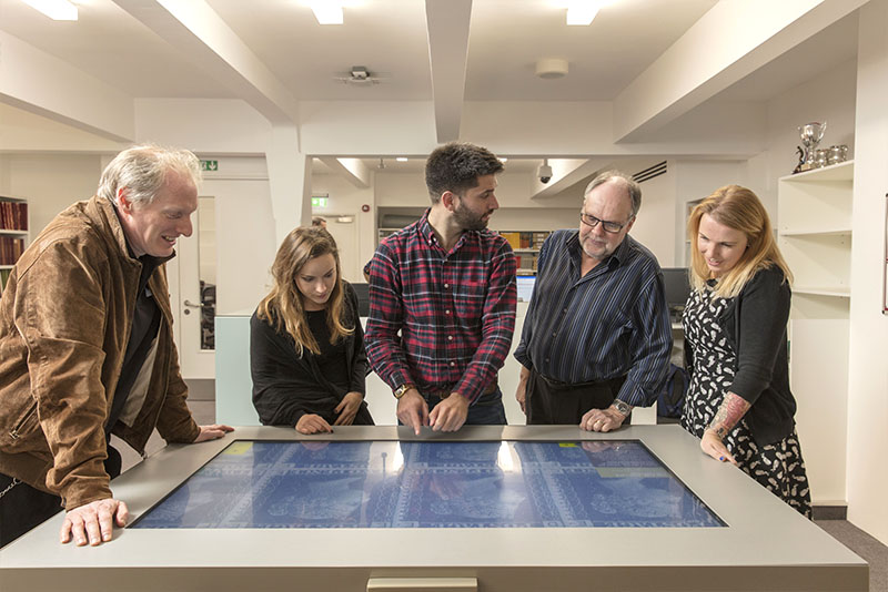 A group of visitors looking at close-ups of Victorian Stamps on the touch table