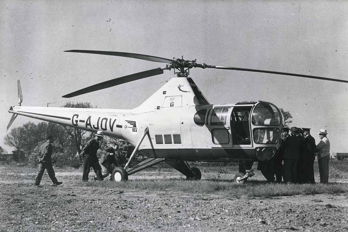 A black and white photo of a Helicopter mail trial in Norfolk. Postal staff surround a helicopter.