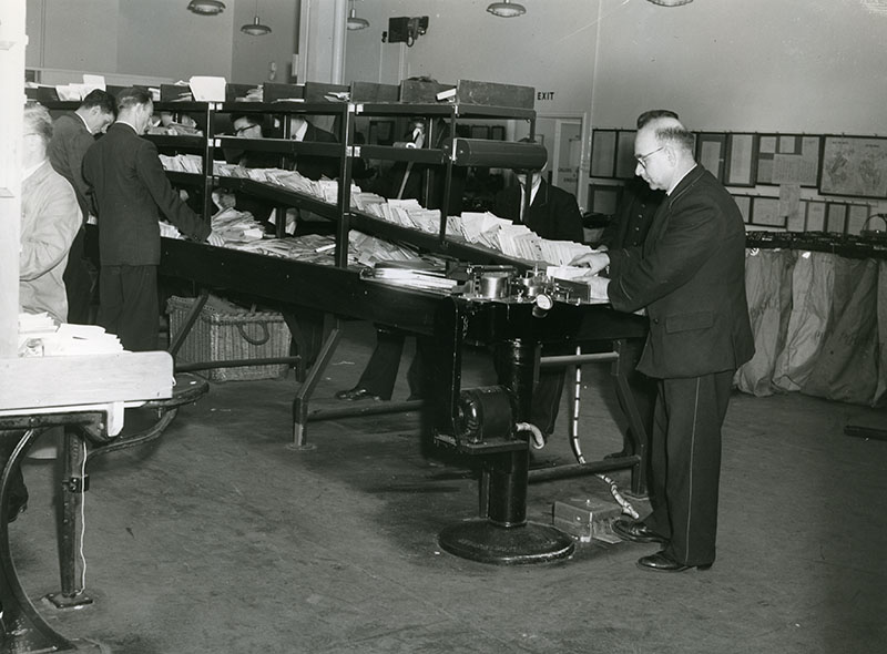 Photo of sorters at stamp cancelling machine, 1957 (POST 118/5248)