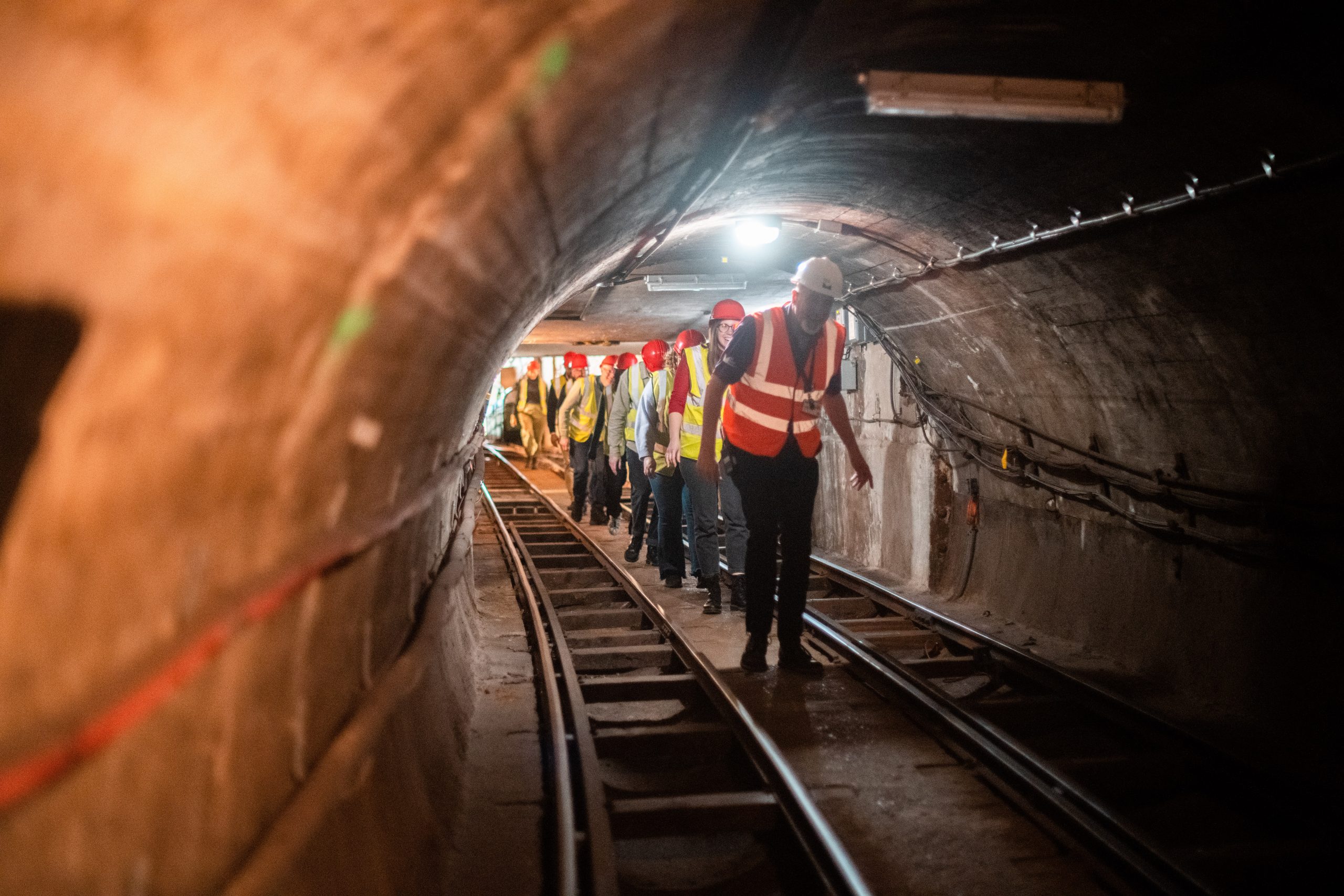 Warwick the tour guides leads tour-goes, wearing high-vis jackets and hard hards, down the cramped Mail Rail tunnel. Some visitors have to duck so they don't hit their heads.