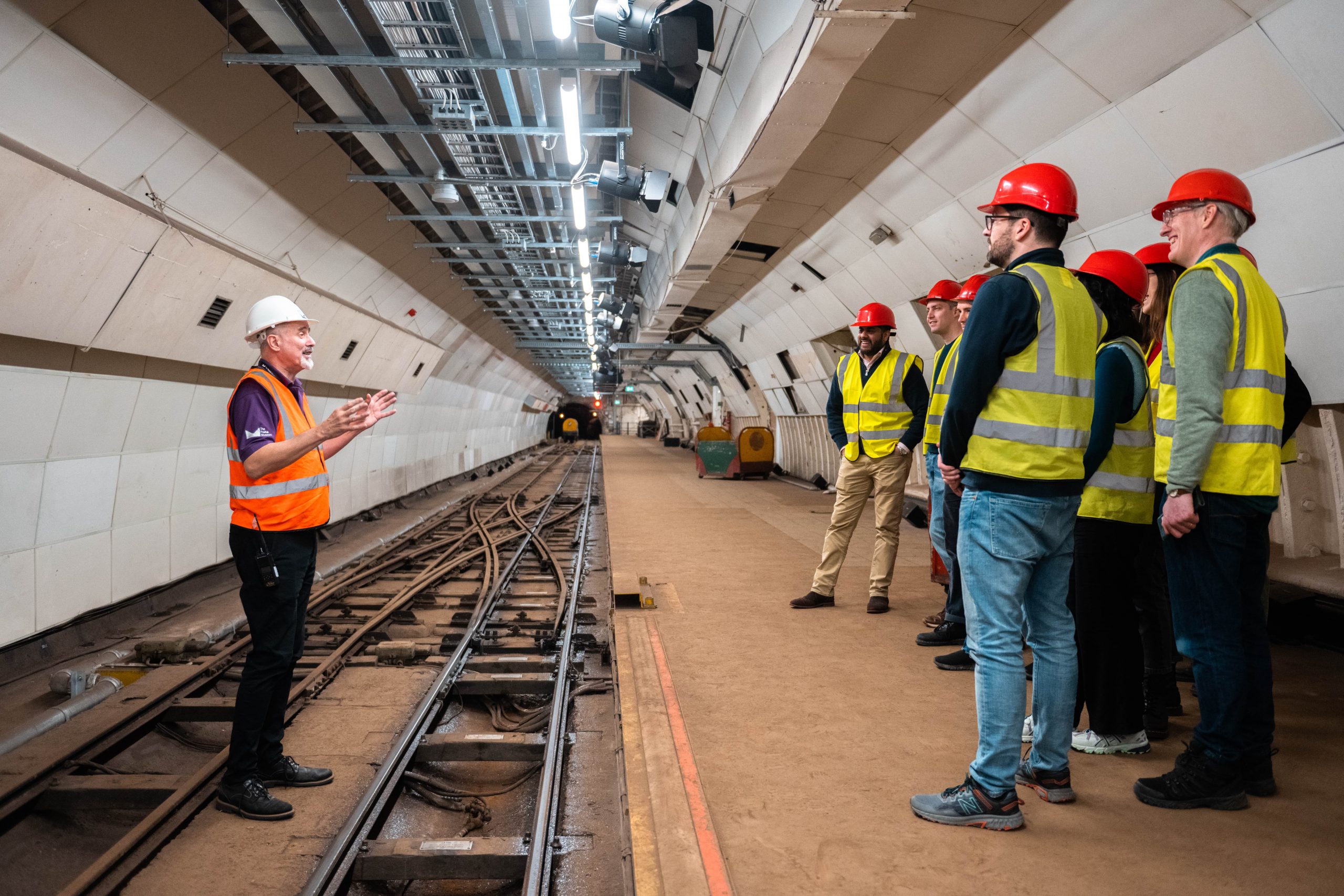 The Tunnel Walks tour guide explains the history of the Mail Rail to engaged visitors, stood on the Mail Rail platform