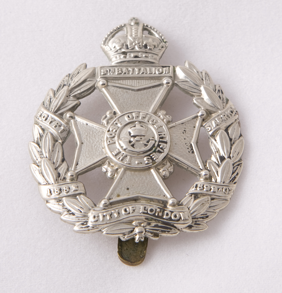 A silver metal badge for the Post Office Rifles consisting of a central cross circled by a laurel wreath.