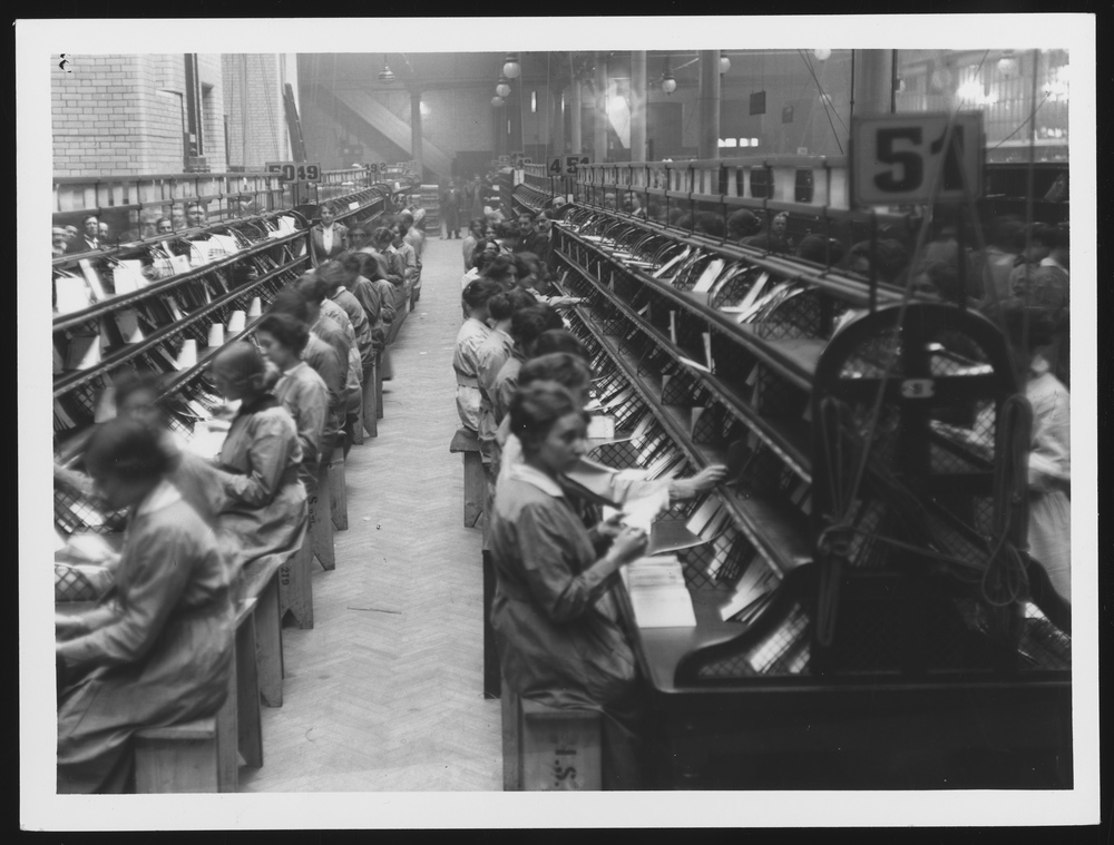 Photograph of numerous women sat in rows sorting letters.