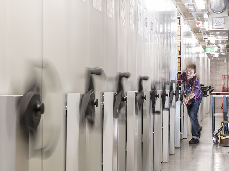 Photograph of a curator moving the shelves of records in The Archive Repository at The Postal Museum.