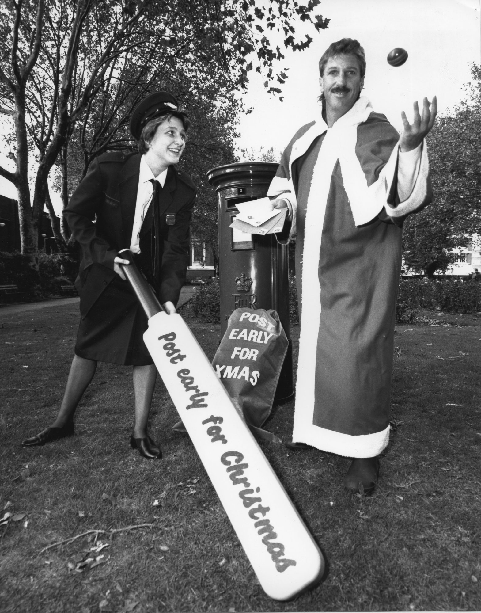 A black and white photograph with a postwomen holding a large cricket bat and Ian Botham dresses as Santa.