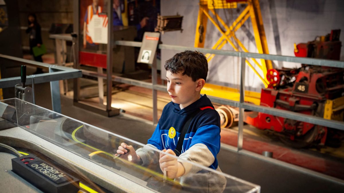 Young boy plays with an interactive exhibition. He is small with dark hair and a blue t-shirt on. He is concentrating on his activity.