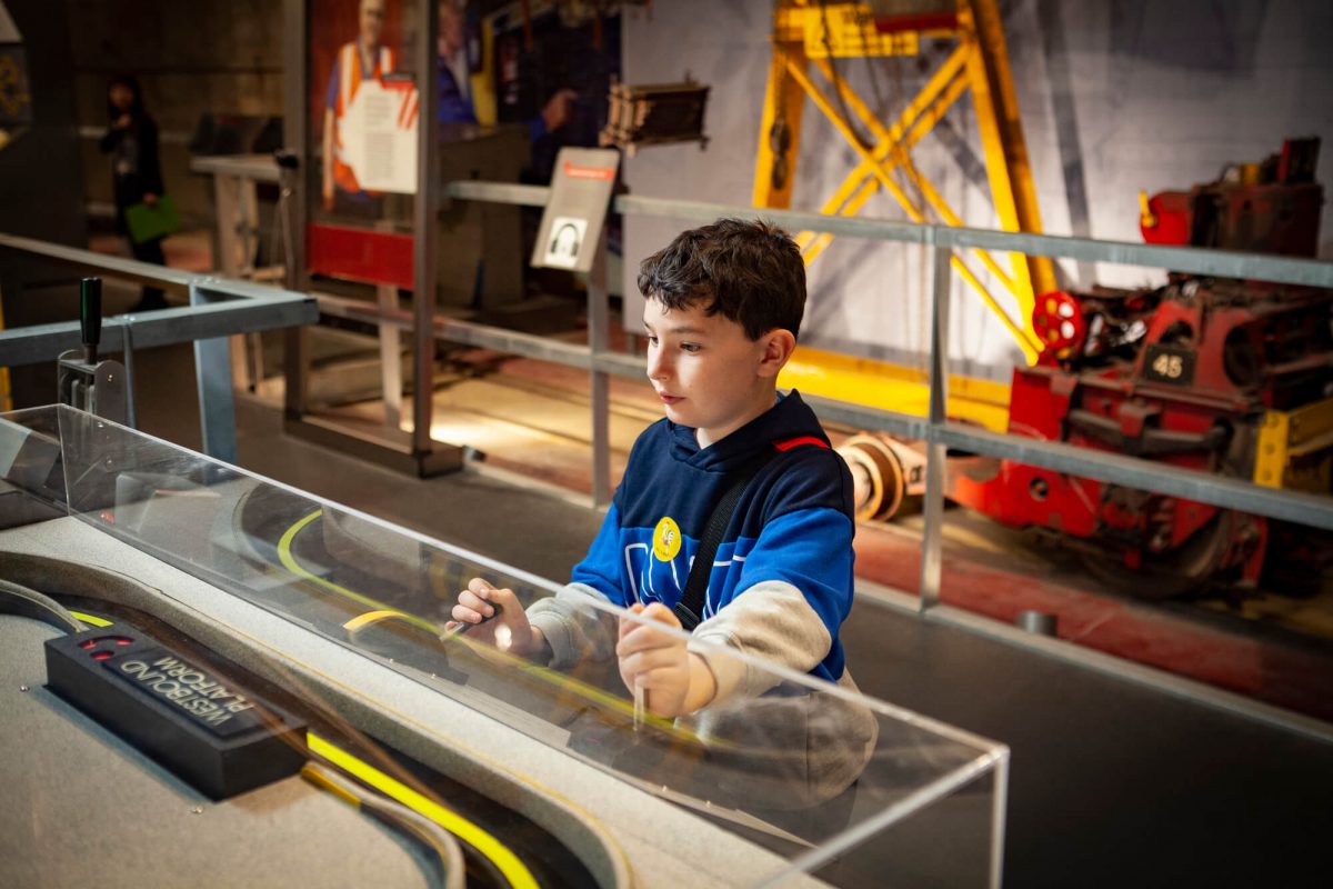 Young boy plays with an interactive exhibition. He is small with dark hair and a blue t-shirt on. He is concentrating on his activity.