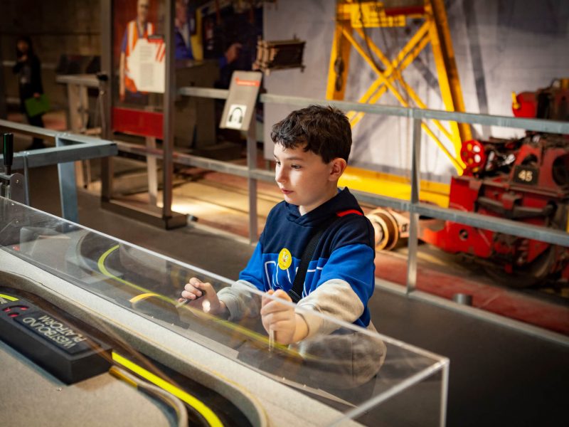Young boy plays with an interactive exhibition. He is small with dark hair and a blue t-shirt on. He is concentrating on his activity.