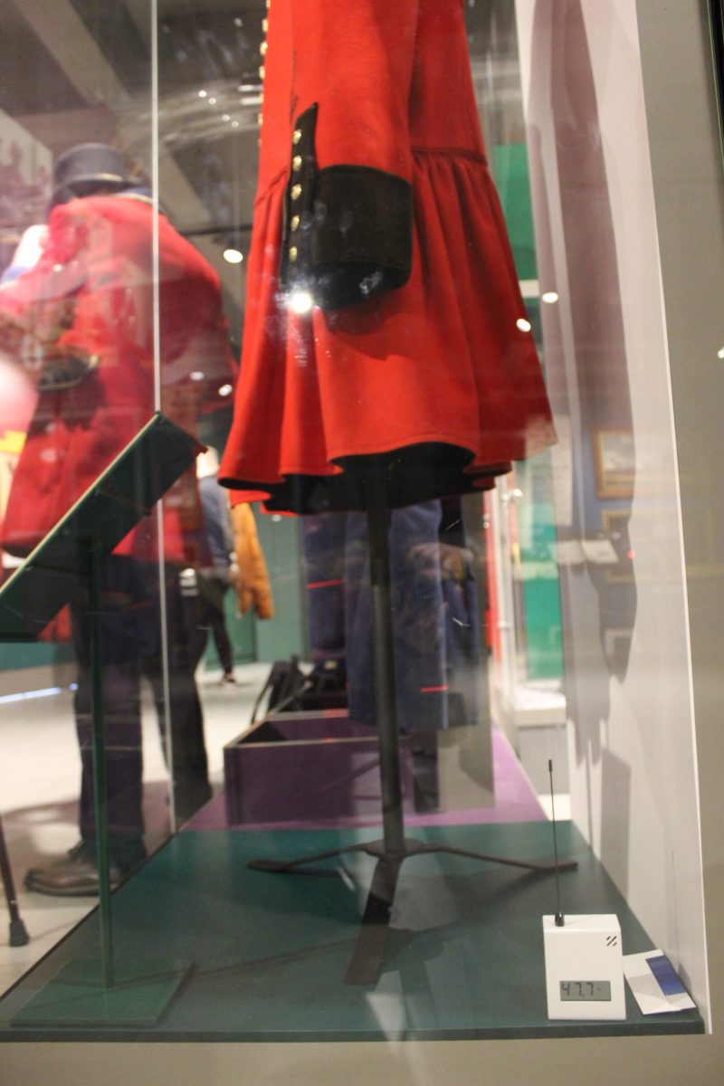 Environment sensor which is a small square box in the bottom right hand corner of a display case. The case includes a red River Postman’s frock coat with black cuffs.