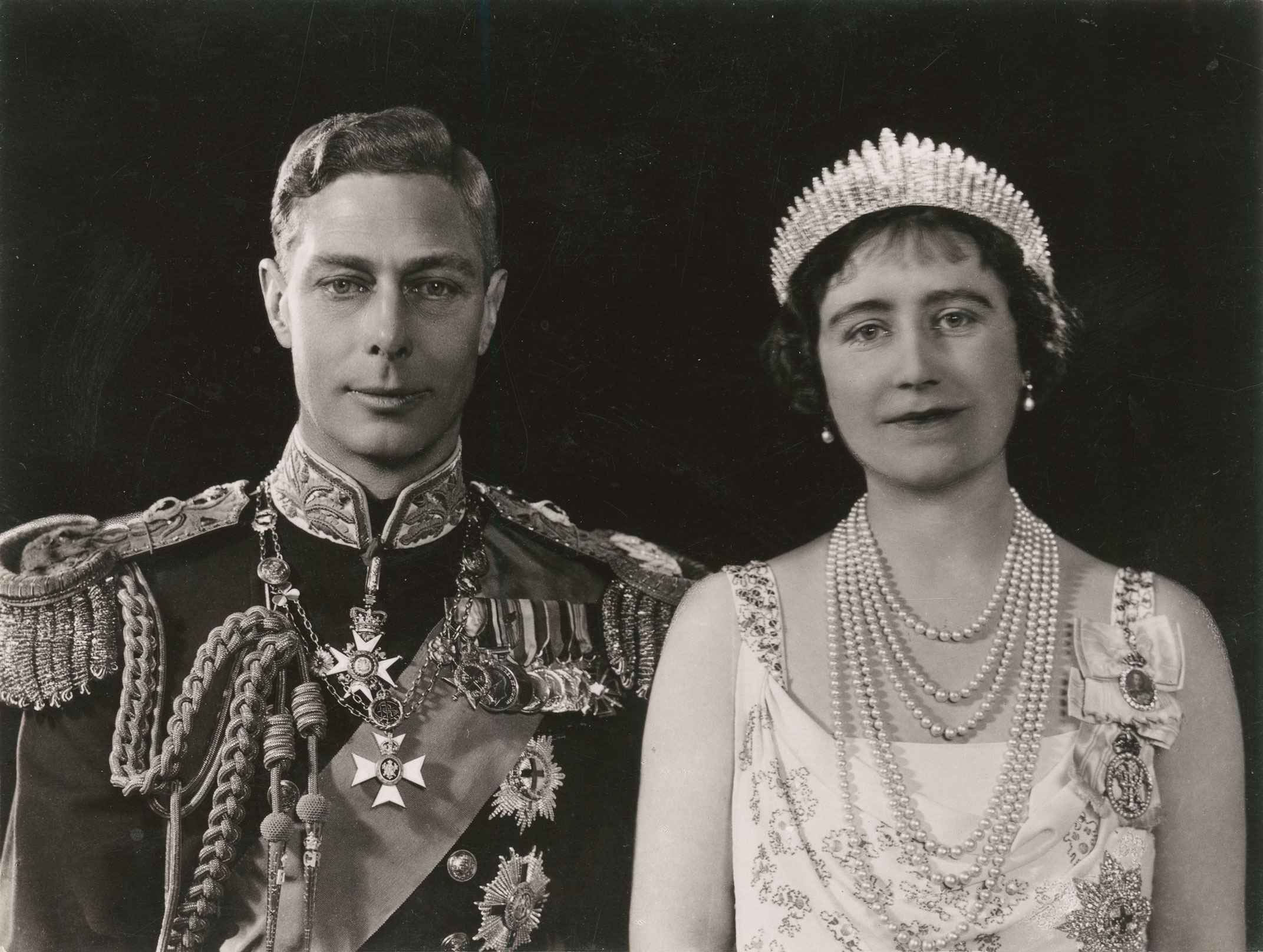 Black and white portrait of the couple side by side. The King wears medals and the Queen pearls and a tiara. 