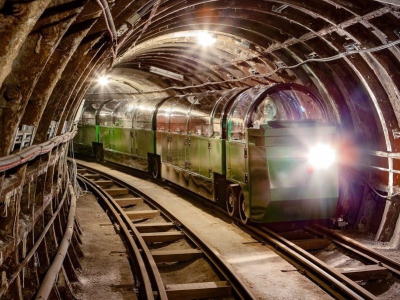 Mail Rail train on tunnel moving towards the camera. The train is green with a glass ceiling and a strong light at the front.