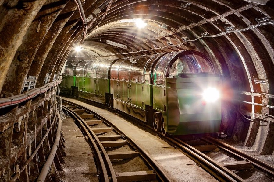 Mail Rail train on tunnel moving towards the camera. The train is green with a glass ceiling and a strong light at the front.