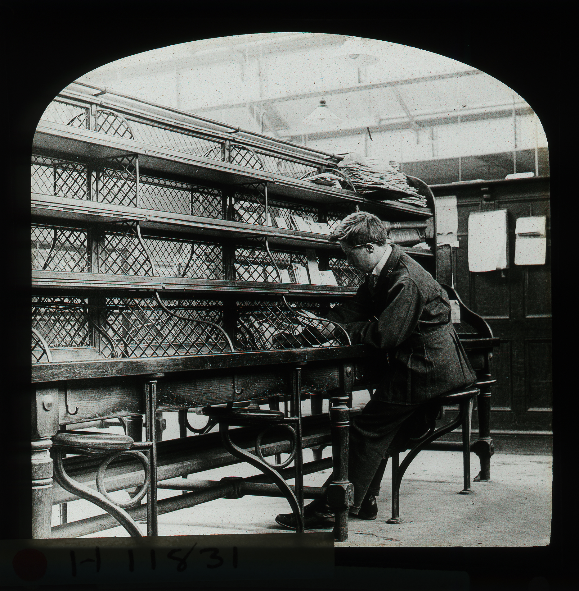 Black and white image of a men working at a desk with shelves above him.