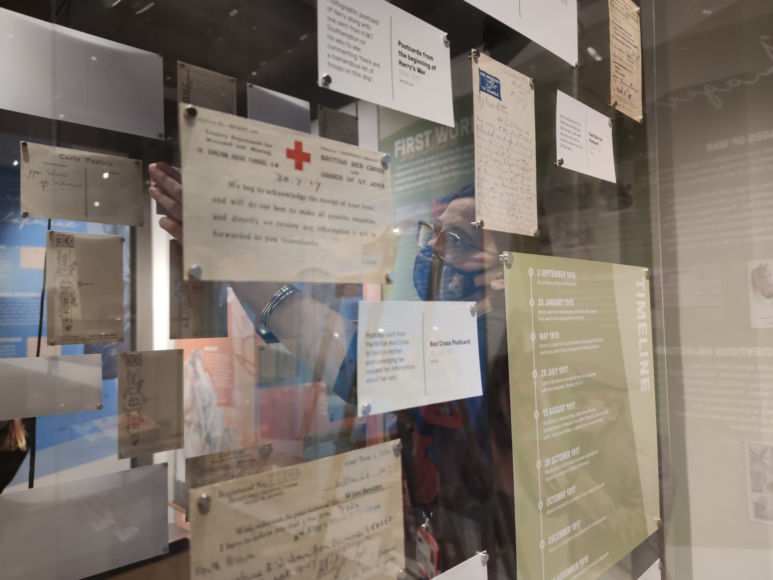 Image of a woman wearing a mask reaching inside a display case where postcards are displayed on magnets.