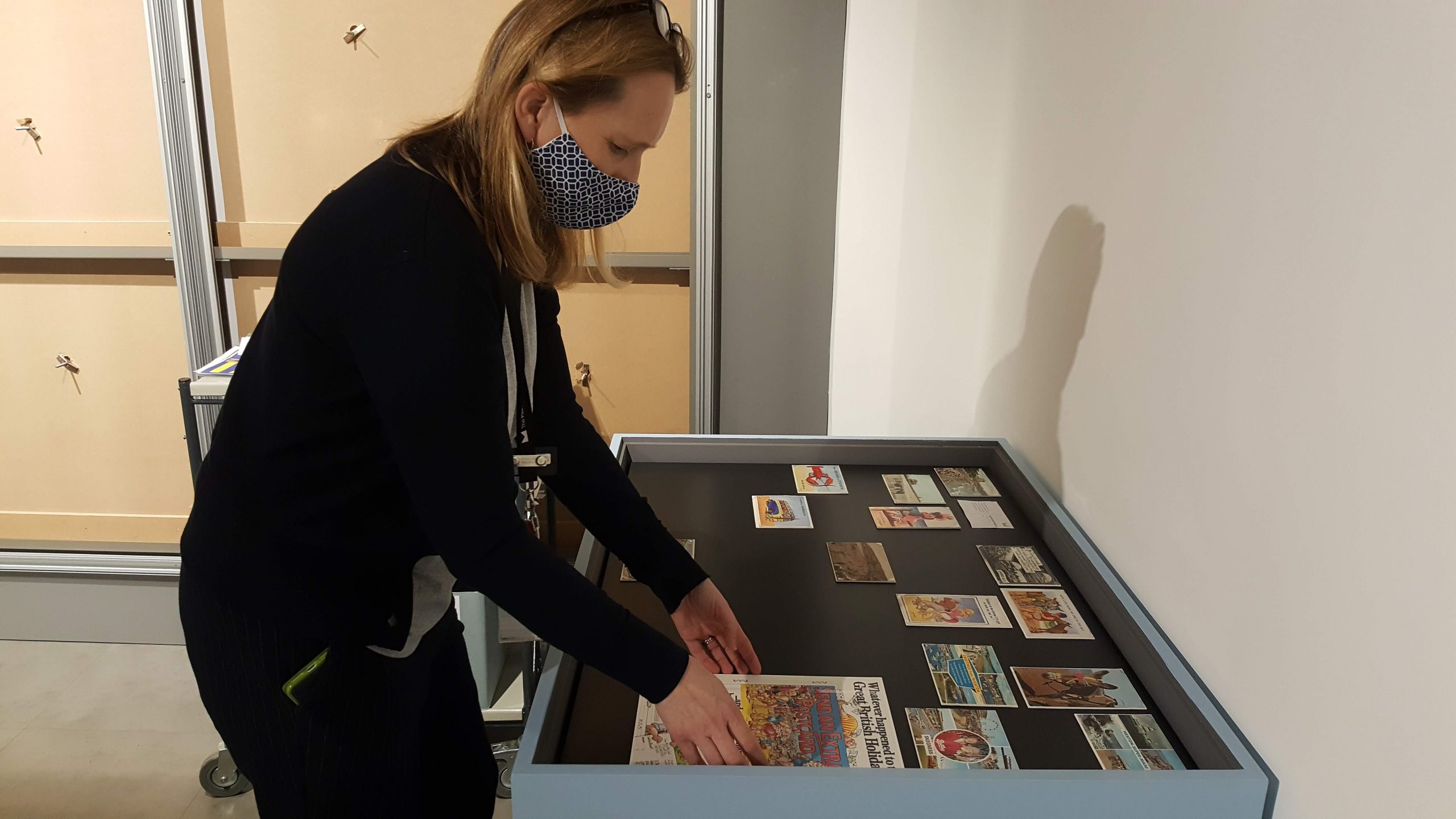 Image of a woman wearing a mask placing a poster into a display case. 
