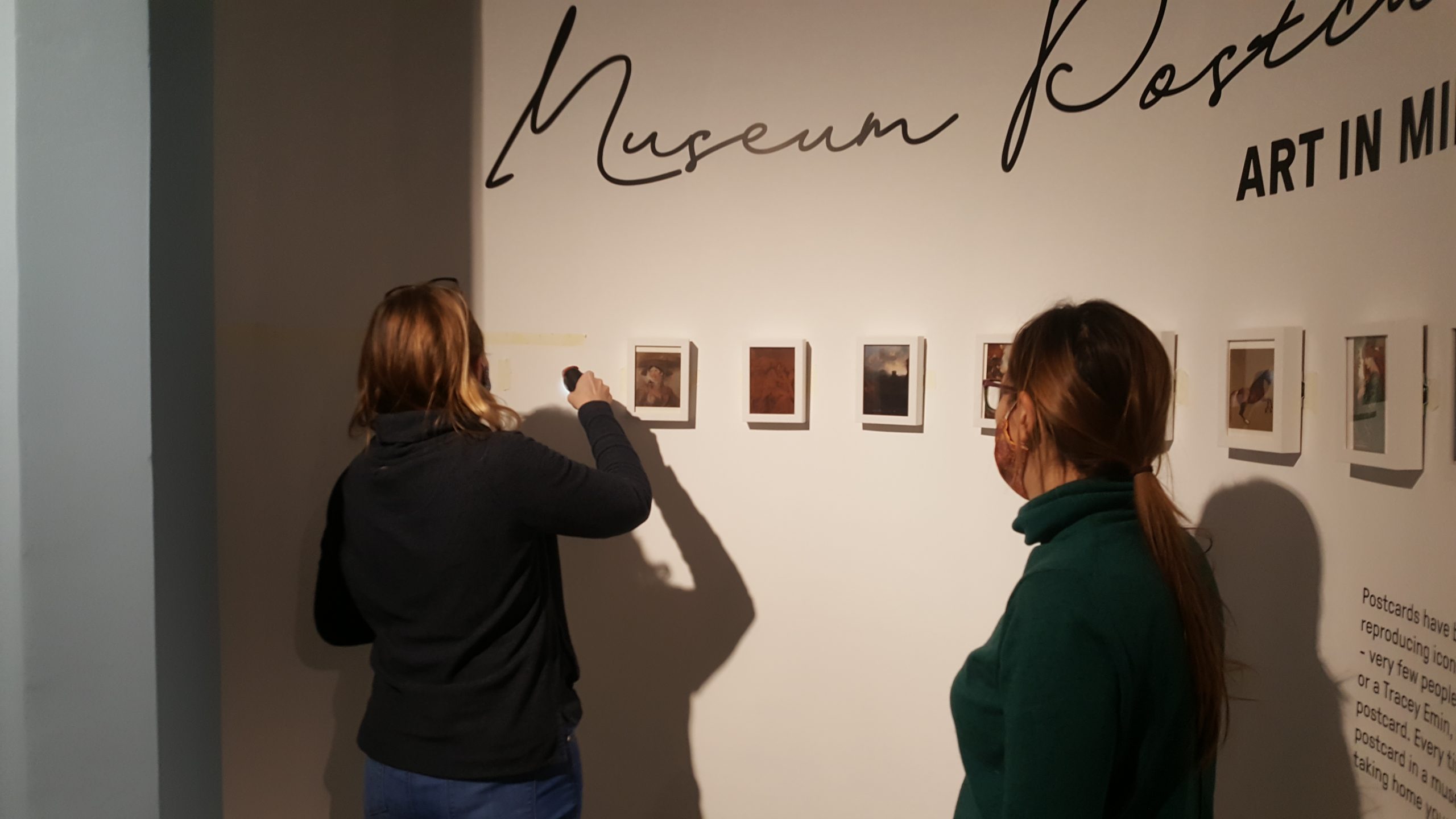 Image of two women wearing masks, where one is drilling into a wall and the other watching. 