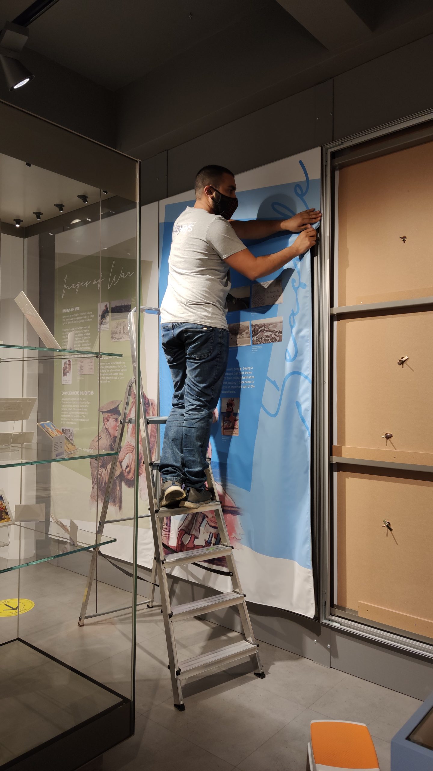 Image of a man on a ladder installing a graphic panel onto the wall. 