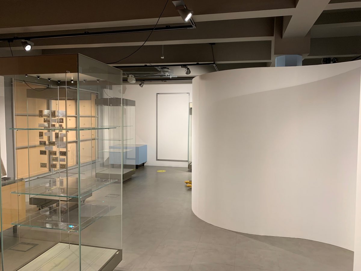 Photograph of a white curved wall and empty display cases within the exhibition area. 