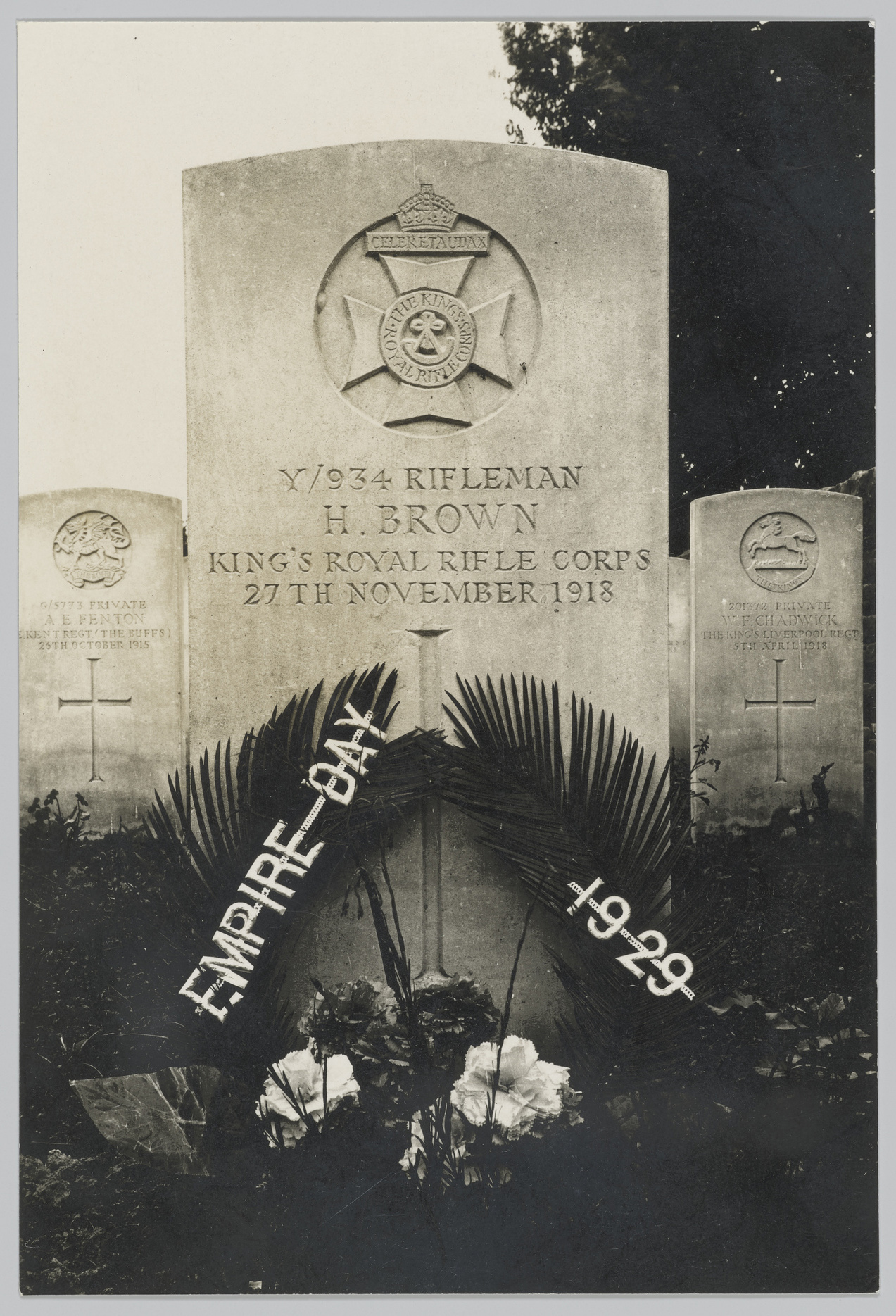 A black and white photograph of Harry Brown's grave with the insignia of his regiment engraved into the grave stone and flowers placed infront. 