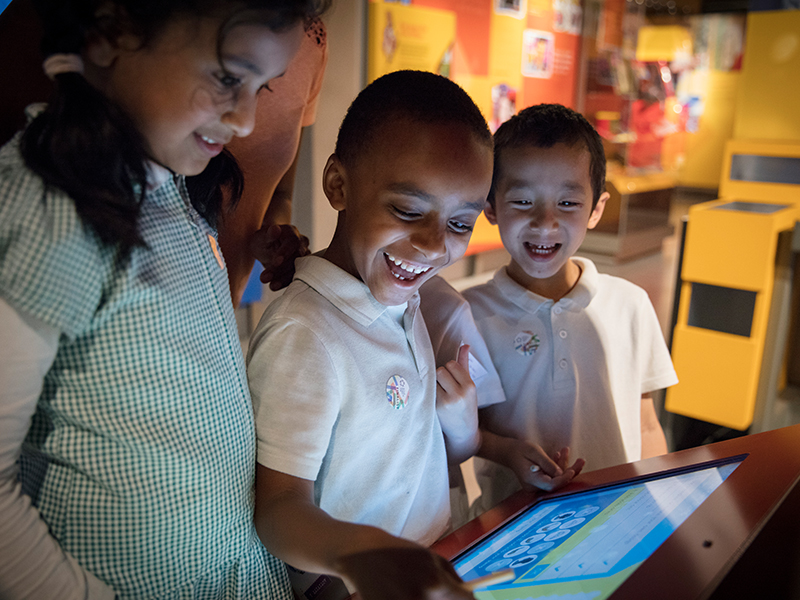 Photo showing school children playing on interactive screens in the museum gallery.