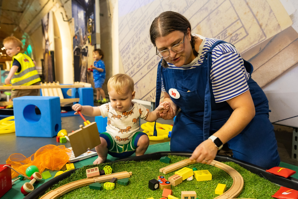 Our Post and Play facilitator helps a young child play with our miniature train set.