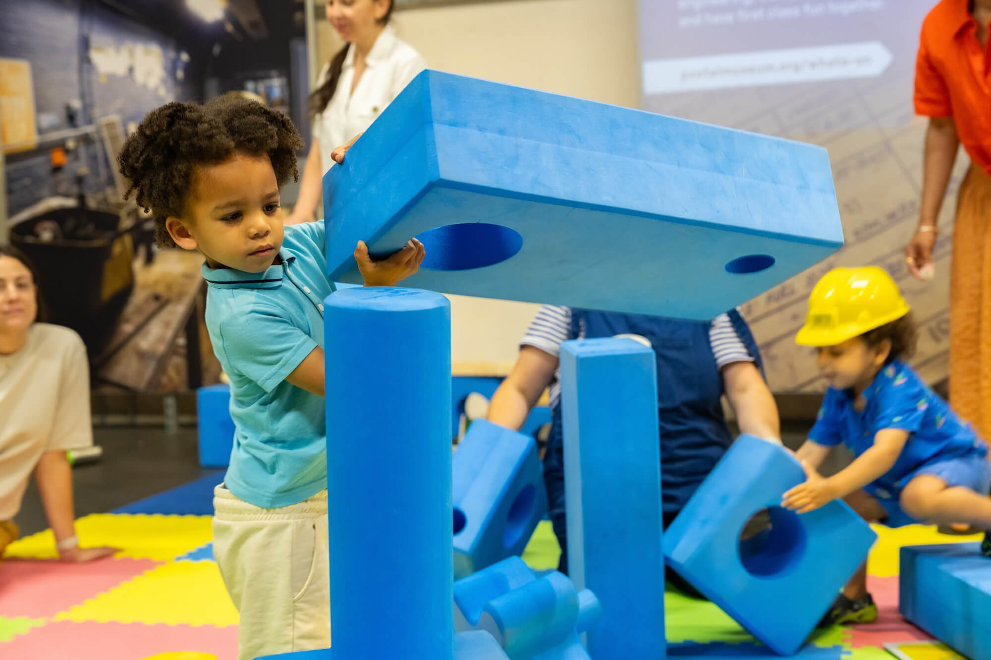 A toddler playing with big blue foam blocks on a play mat.