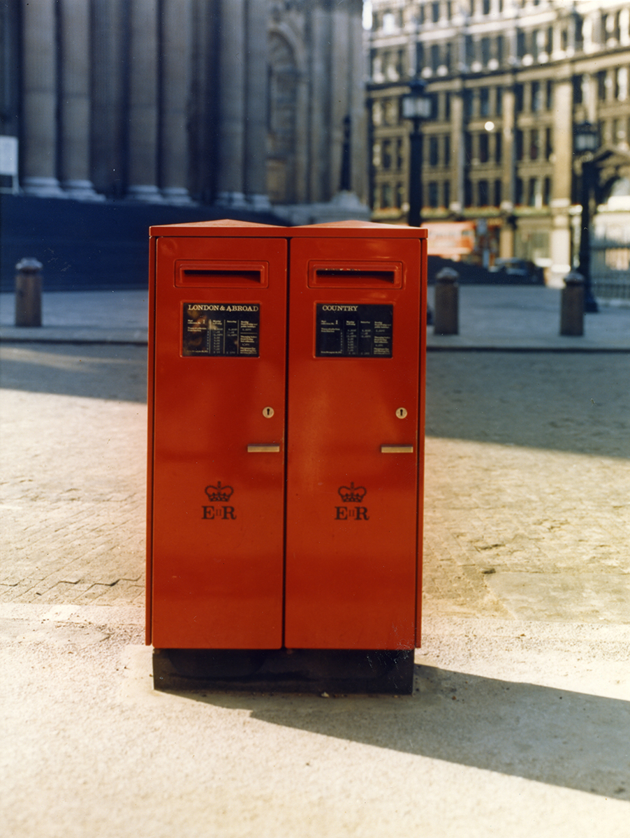 Photograph. Image orientation: portrait. Colour. Photograph taken near St Paul's Cathedral, London. Showing a red, double aperture letter box on a London street. Photo taken from the front. The front of each letter box has a cypher with the letters 'ER' to represent Queen Elizabeth II.