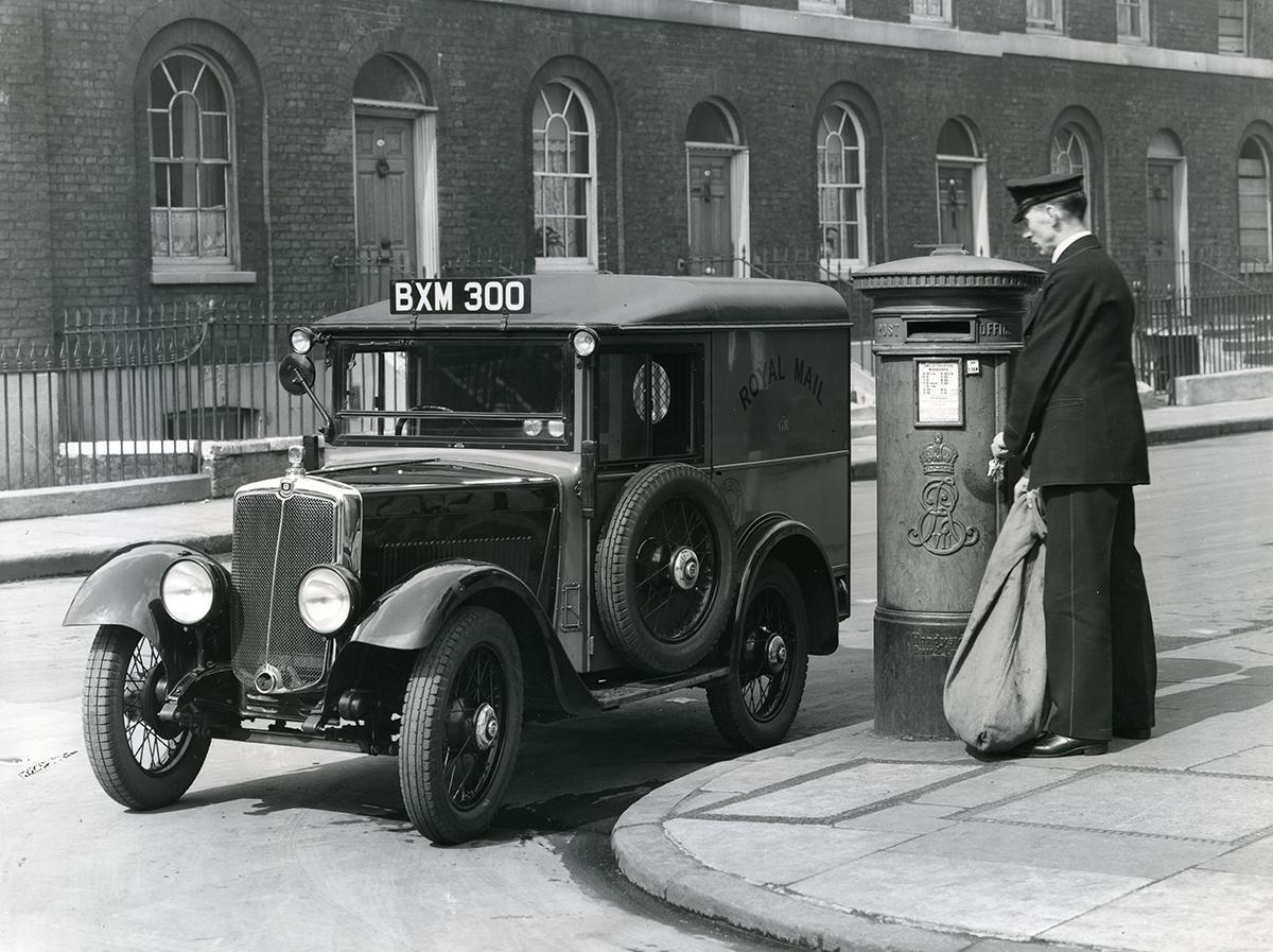 Photograph. Image orientation: landscape. Black and white. A postman collecting a sack of mail from a pillar box, standing in front of a Royal Mail van, registration number 'BXM 300'.
