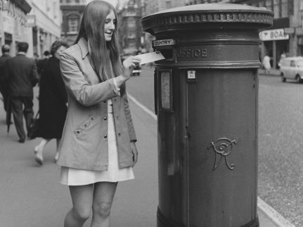 A woman posting a letter into a pillar box, in an unidentified London street.