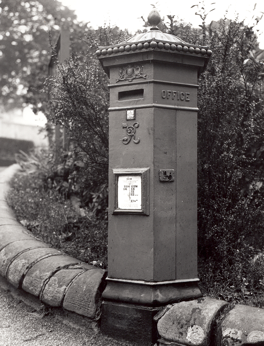 An old six-sided letter box, standing on the side of a curved pathway.