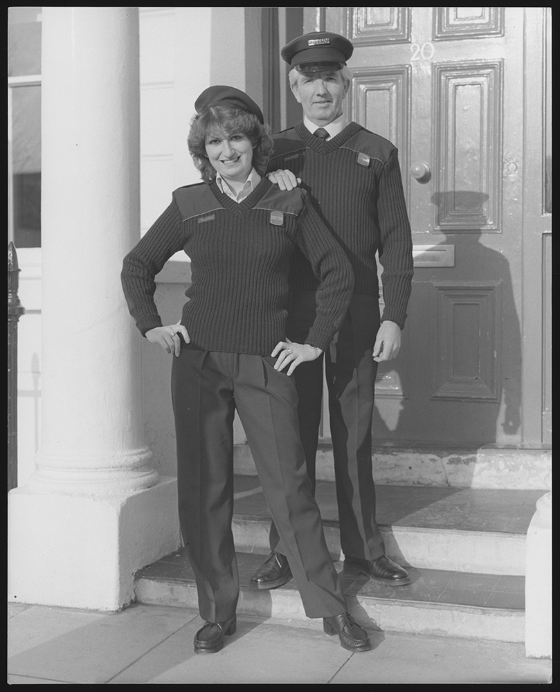 Photograph. Image orientation: portrait. Black and white. Two postal workers (one female, one male), posing on a front doorstep.