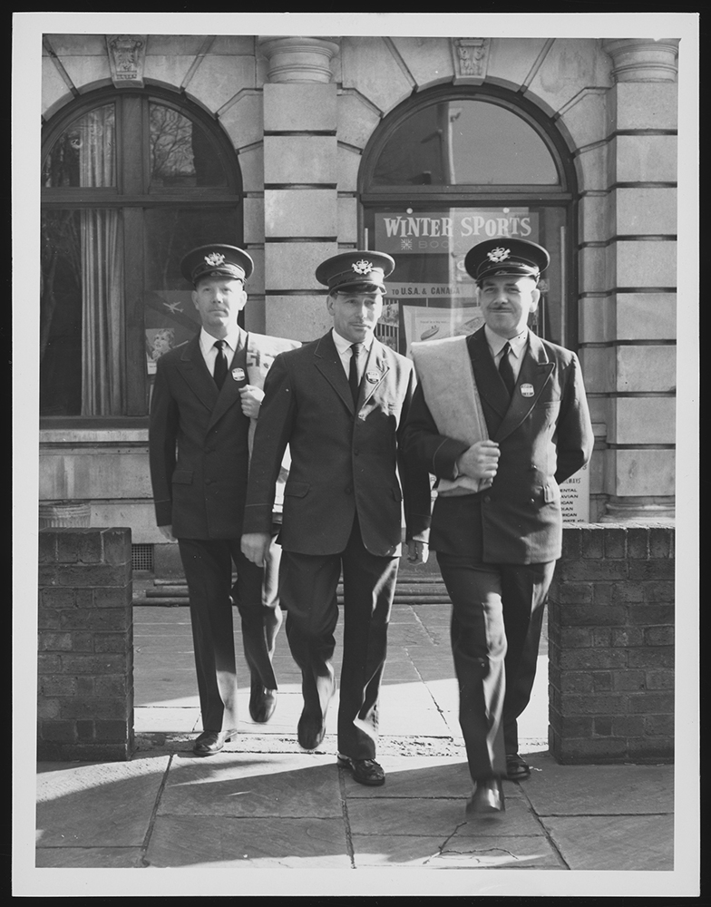 Photograph. Image orientation: portrait. Black and white. Three postmen in uniform.
