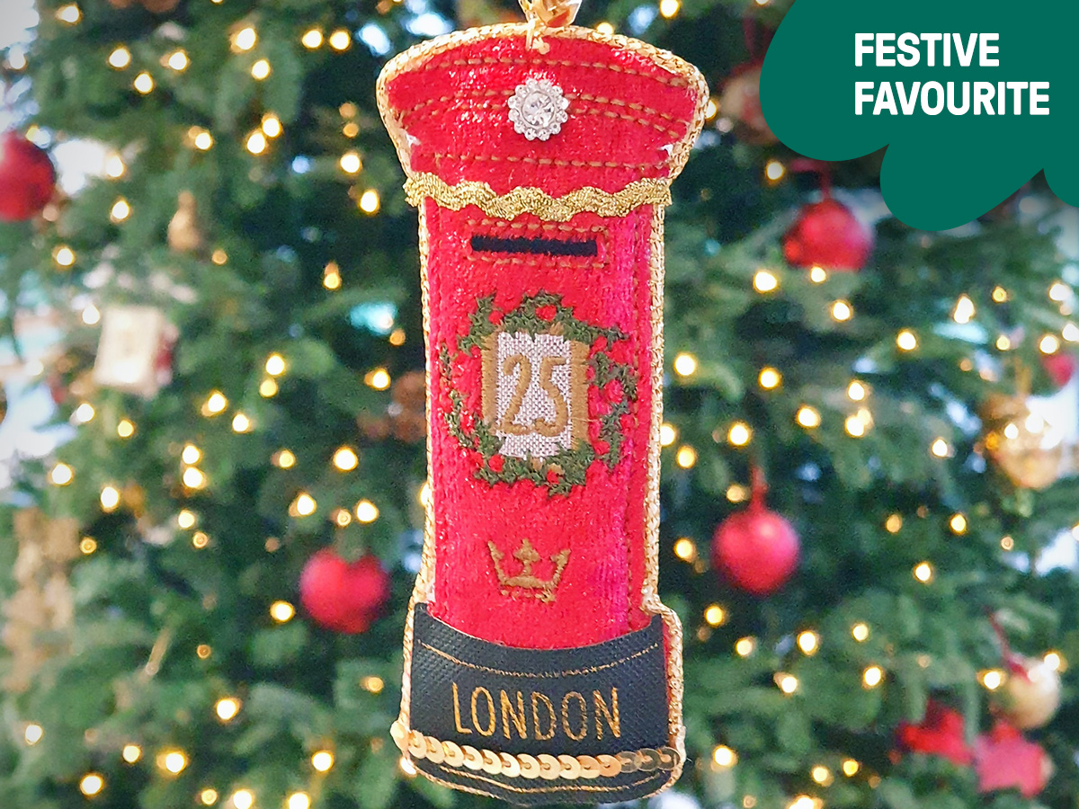 Photograph showing a red and gold fabric decoration handing from a Christmas tree, in the shape of a traditional UK pillarbox.