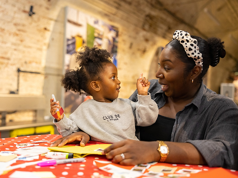 Photo of a parent and child playing with arts and crafts materials at a table in the Mail Rail depot.