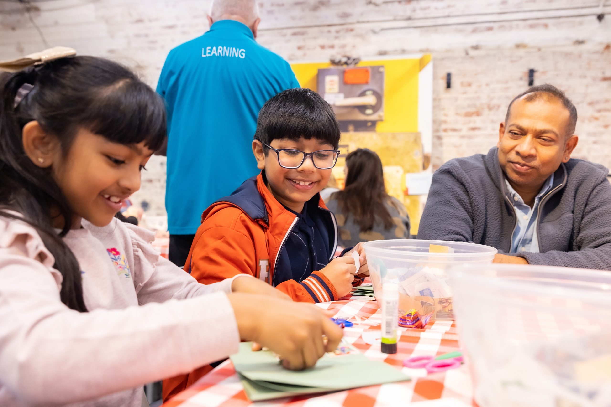 Two smiling young people are sticking stamps down with glue while their father watches