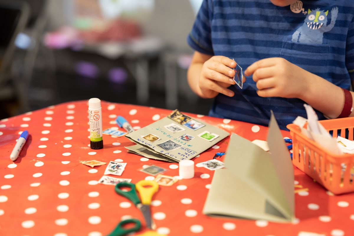 An arts and crafts station showing little hands gluing stamps onto brown paper