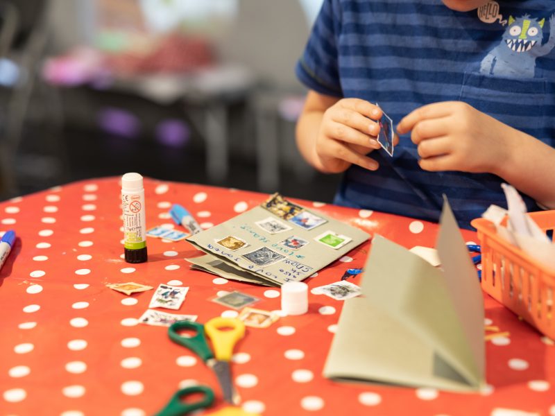 An arts and crafts station showing little hands gluing stamps onto brown paper