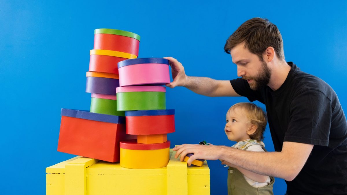 Father helps his young son stack multi-coloured building blocks as part of the Post and Play activities