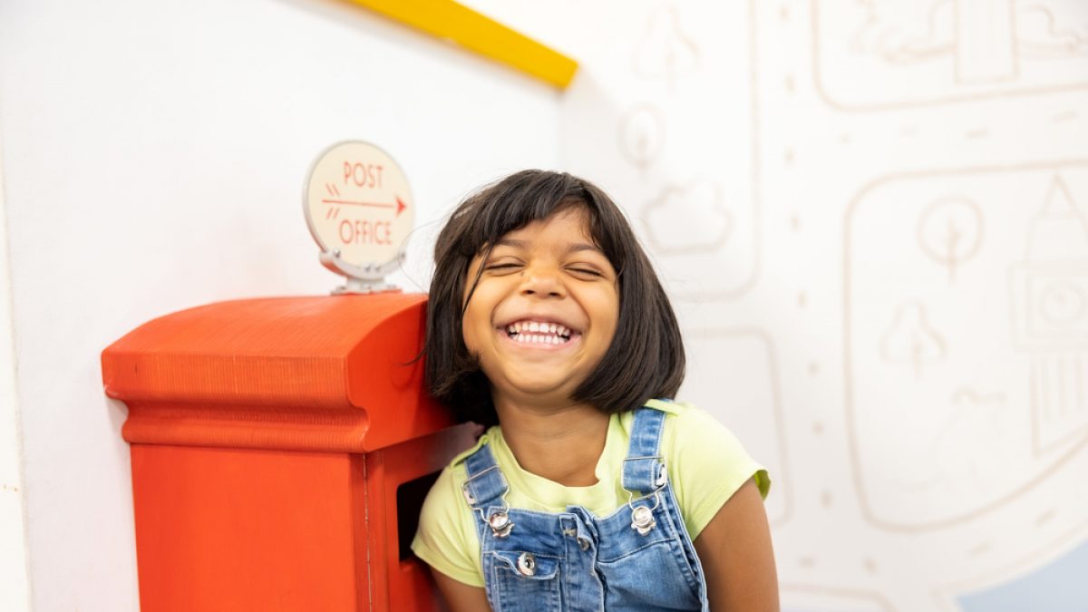 Small child looking very happy whilst playing in our Sorted play space. She is wearing denim dungarees and a yellow t-shirt.