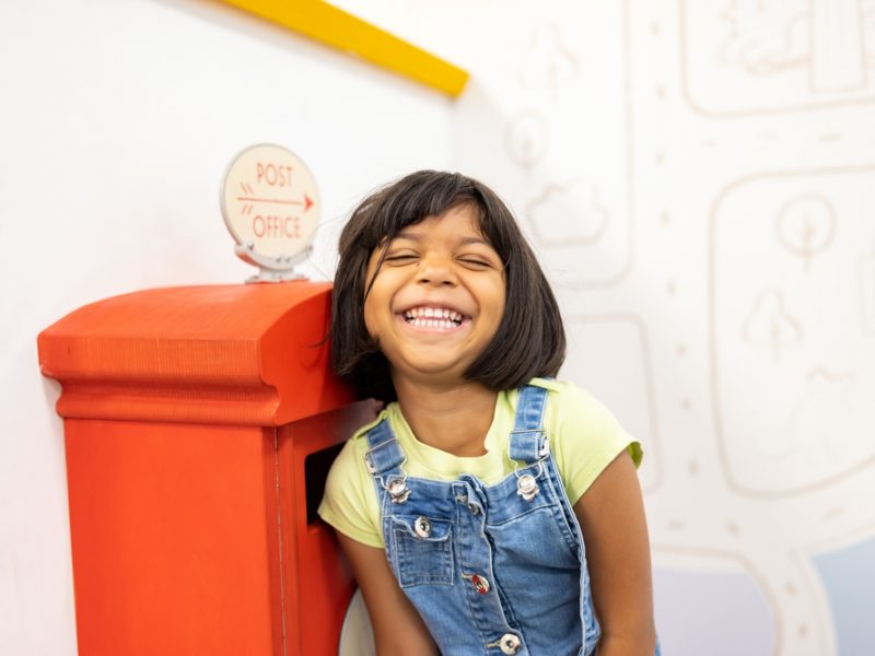 Small child looking very happy whilst playing in our Sorted play space. She is wearing denim dungarees and a yellow t-shirt.