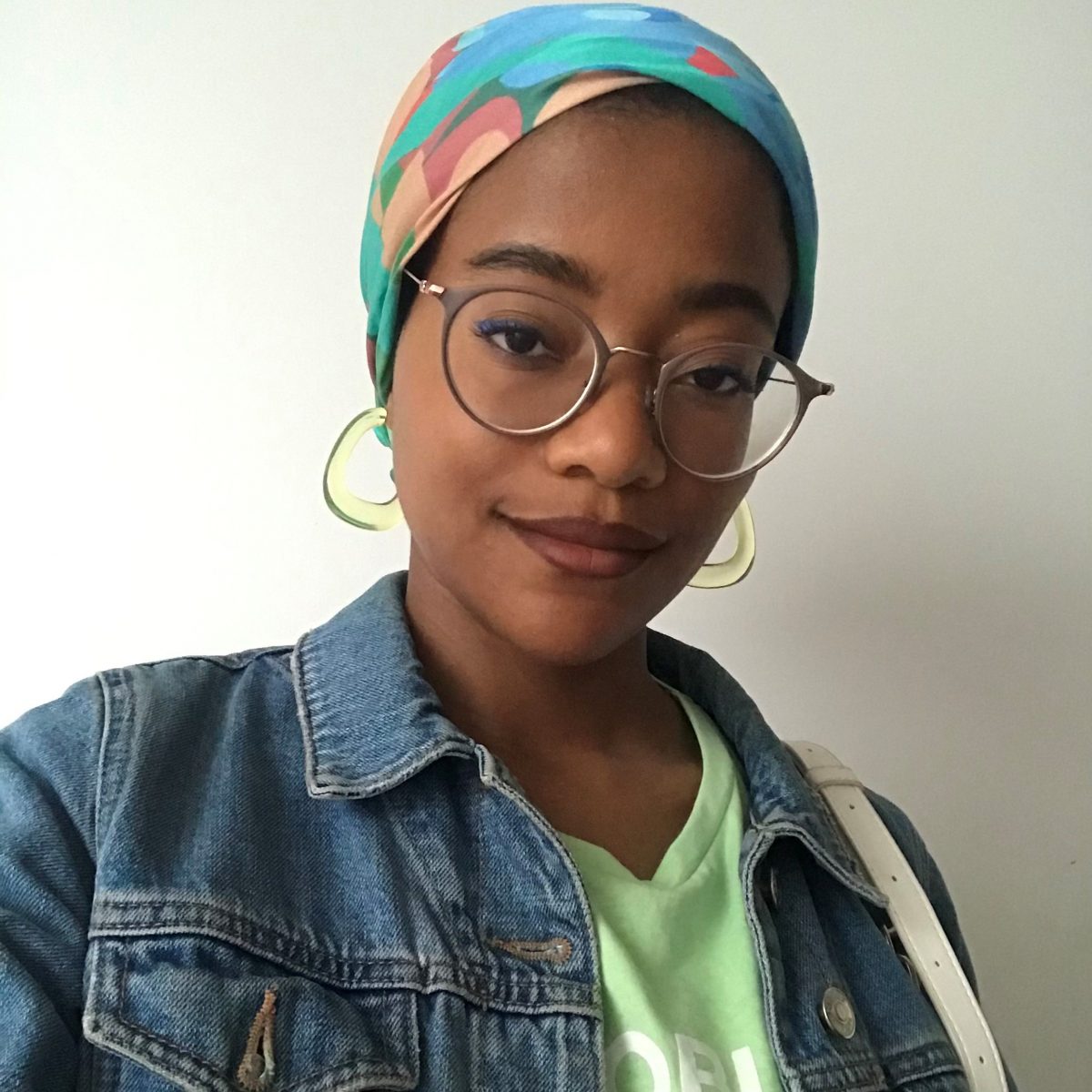 This is a selfie of the artist Bokiba. She looks to be in her twenties and is wearing big hooped earrings, glasses and a colourful bandana. 