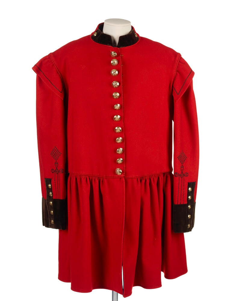 A very formal, bright red 'frock coat', worn by Postmen. It has dark red, velvet cuffs and collar, and gold buttons down the middle and up the sleeves. The bottom is quite frilly, almost like the hem of a dress. 