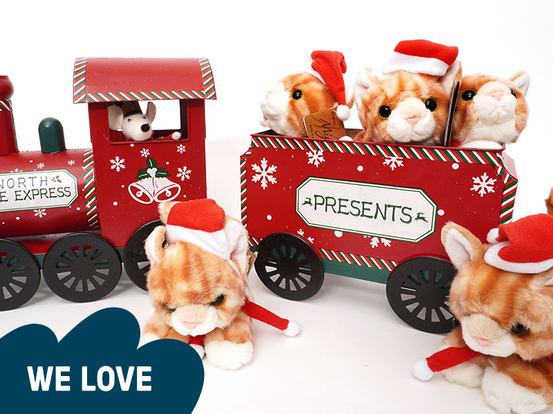 Five fluffy orange toy cats wearing Santa hats, arranged in the carriages of a wooden toy train.