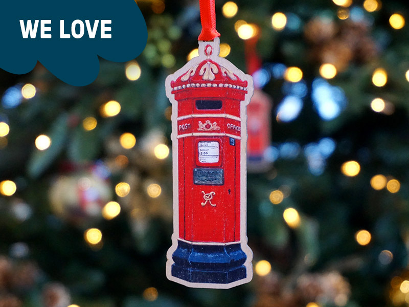 A wooden Christmas decoration with an illustration of an ornate red Victorian pillar box.