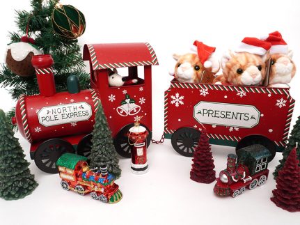 A selection of Christmas gifts on a white table, including a red toy train, fluffy cat toys and tree decorations.